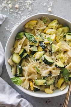 a white bowl filled with pasta and veggies next to two silver spoons