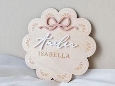 a wooden name tag with a pink bow on it's side and the word hello is abaella written in cursive writing