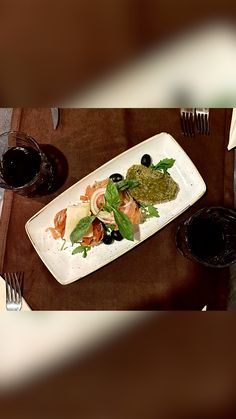 a white plate topped with lots of food next to two glasses of red wine on top of a wooden table