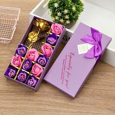 a purple box filled with pink roses next to a potted plant on top of a wooden table