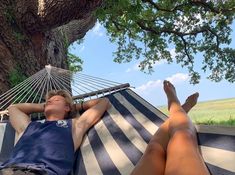 a man laying in a hammock under a tree with his feet propped up