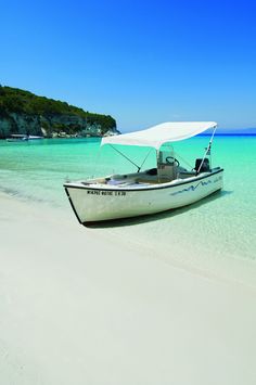 a small boat is parked on the beach in clear blue water, with an island in the background