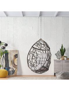 a hanging chair in the middle of a room with plants and pictures on the wall