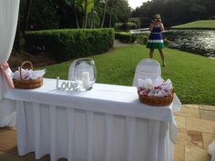 a woman standing next to a table with flowers and candles on it in front of a lake