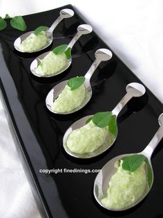 four spoons filled with ice cream on top of a black serving tray and green leaves