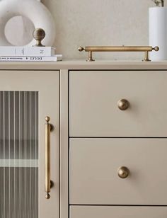 a white dresser with gold handles and knobs on it's drawers next to a clock