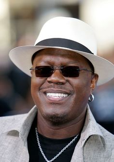 a man wearing sunglasses and a hat smiles at the camera while standing in front of a crowd