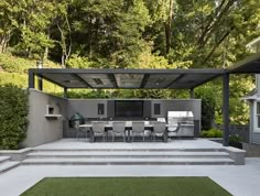 an outdoor kitchen and dining area with grass in the foreground, surrounded by trees