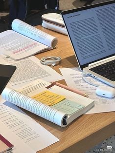 an open laptop computer sitting on top of a wooden table next to books and papers