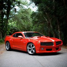 a red sports car is parked on the side of the road in front of some trees