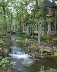 a house in the woods with a stream running through it's front yard area