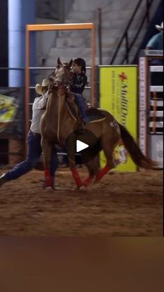 a woman riding on the back of a brown horse in an indoor arena at night