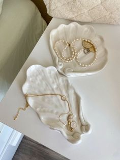 two white shell shaped trays with pearls on them sitting on top of a table