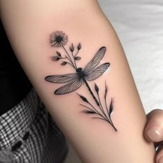 a woman's arm with a dragonfly and flowers tattoo on the left forearm