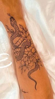 a tattoo on the leg of a person with a snake and flowers in it's arm