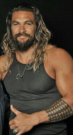 a man with long hair and tattoos on his arm, wearing a black tank top