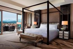 a bedroom with a four poster bed and an ottoman in front of large windows overlooking the mountains