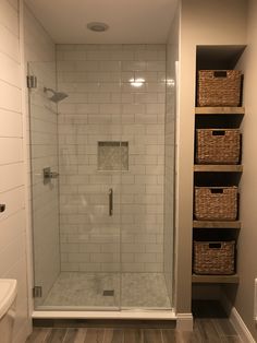 a walk in shower sitting next to a white sink and wooden shelves on the wall