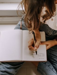 a woman sitting on the floor writing in a notebook with a pen next to her