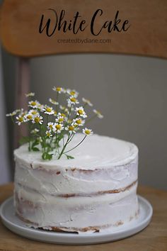 a white cake sitting on top of a wooden table next to a plate with flowers