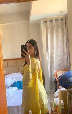 a woman taking a selfie in front of a mirror while wearing a yellow dress