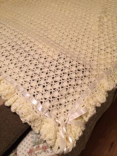 a white crocheted blanket on top of a bed with lace and ribbon around the edges