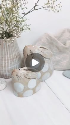 a vase filled with flowers next to two ceramic rabbits on top of a white table