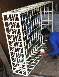 a man kneeling down in front of a white metal cage holding a cup and container