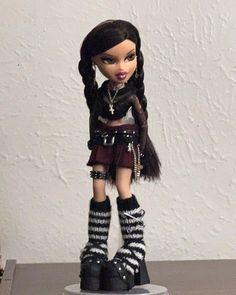 a doll with black hair and boots on top of a table in front of a white wall