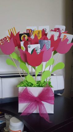 a bouquet of paper flowers in a white box with pink ribbon on a desk next to a printer