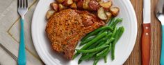 a white plate topped with meat and potatoes next to green beans on a wooden table