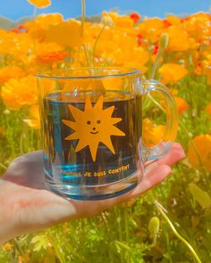 a person holding a glass cup with a sun on it in a field of flowers