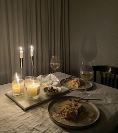 a table topped with plates of food next to glasses of wine and candlelight candles