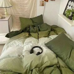 an unmade bed with green sheets and headphones on it in a white room