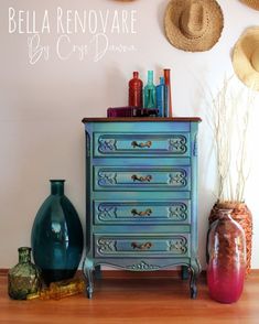 a blue dresser sitting on top of a wooden floor next to vases and hats