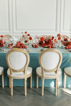 the table is set with white chairs and red centerpieces on top of it