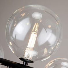 three clear glass globes are hanging from a black metal light fixture on a white wall