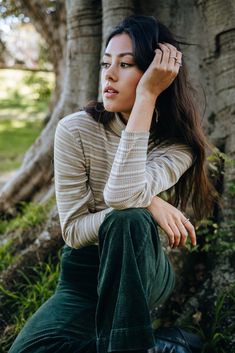 a woman sitting in front of a tree with her hand on her head and looking off to the side