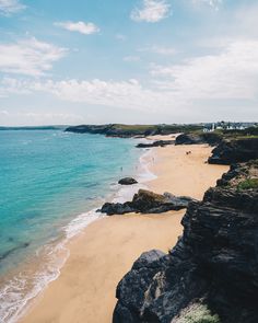 a sandy beach next to the ocean under a blue sky with some clouds in the background