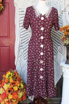 Beautiful floral acetate/rayon dress bestowing white flowers on a burgundy background make this dress a perfect tea party, garden party dress, for office, secretary, academia, church wear, etc.! Dress bestows a v-neckline with lacey off white collar, padded shoulders, short sleeves, large pearly front button closure, has a lace up back for a more fitted waist style that flares out around hips and is around calf length depending on your height. Dress is in excellent vintage condition showing minimal wear for its age. Please seem all photos as this is part of description. Tag states this as being a size 11 / 1 2, but this is vintage sizing so please check all measurements for best fit. Pictures were taken using a size 8 dress form and it fit this size quite nicely. Measurements are taken wit Ladies Tea Party, Dress For Office, Office Academia, Ladies Tea, Victorian Fashion Dresses, Tee Party, Burgundy Background, Dress Office, 90s Floral