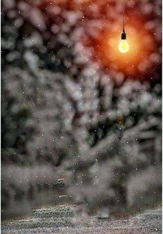 an orange light bulb hanging from the side of a building with snow falling on it