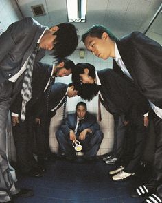 four men in suits and ties sitting on a subway car looking down at the ground