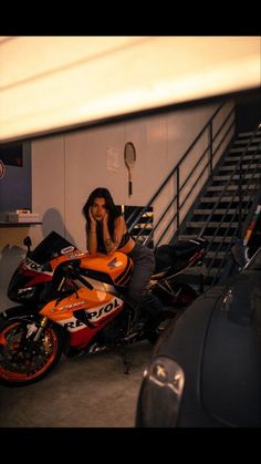 a woman sitting on top of a motorcycle in a garage next to some stairs and railings