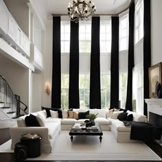 a living room with black and white curtains on the windows, couches, coffee table and chandelier