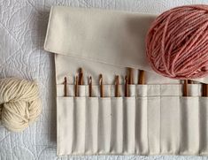 several skeins of yarn and knitting needles on a white quilted surface next to a roll of thread