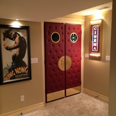 a movie poster hangs on the wall next to a red door in a room with carpeted flooring