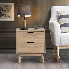 a chair next to a table with a lamp on it and a wooden night stand