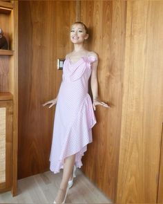 a woman in a pink dress standing next to a wooden wall with her hand on the door handle