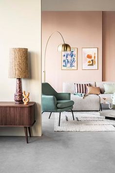 a living room filled with furniture and a lamp on top of a wooden table in front of a pink wall