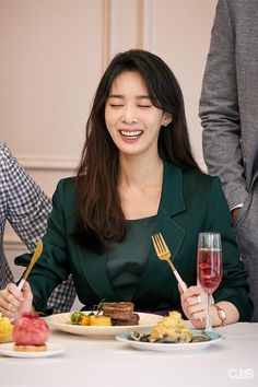 a woman sitting at a table with food and wine in front of her, smiling